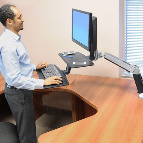 WorkFit-A standing desk with suspended keyboard tray and LCD monitor, providing ergonomic comfort for users.